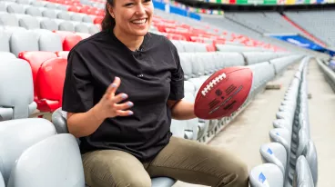 Nadine Nurasyid sitzt auf der Tribüne in der Allianz Arena und hält einen Football in ihrer linken Hand