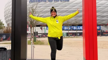 Eine Frau steht in einem überdimensionalen Bilderrahmen, vor der Allianz Arena in München