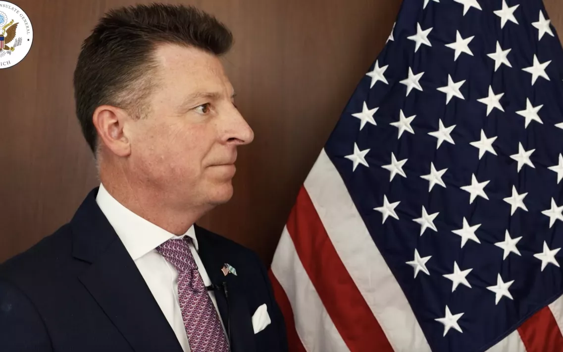 US-Generalkonsul Timothy Liston steht bei einem Video-Interview vor der US-amerikanischen Flagge