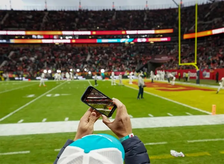 Ein Fan nimmt mit seinem Handy vom Spielfeldrand in der Allianz Arena ein Foto vom NFL Munich Game auf. 