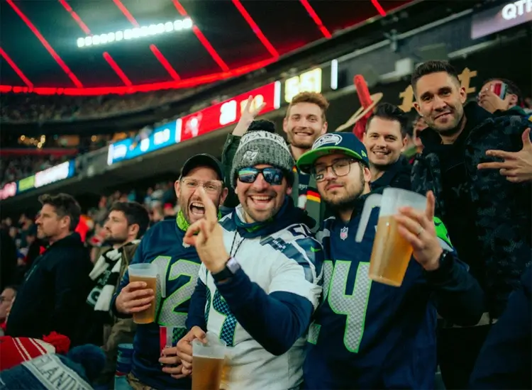 Several fans stand in the spectator area of the Allianz Arena and look forward to the NFL Munich Game. 